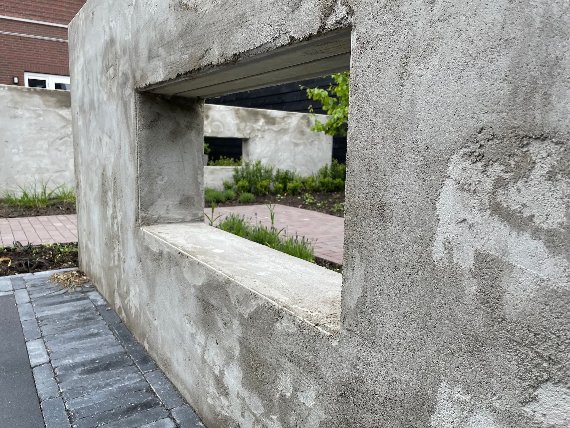 Tuinmuur met doorkijk met groen erom heen.